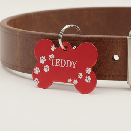 Personalised bone-shaped red dog tag engraved with paw prints and the name Teddy